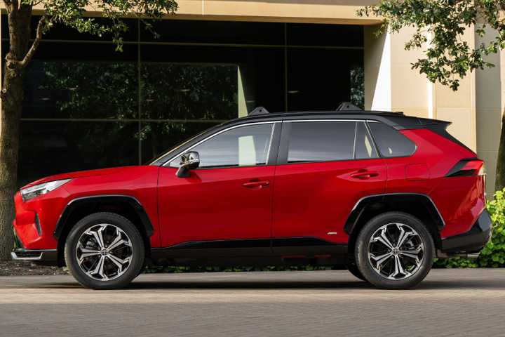 Static side profile shot of a red 2025 Toyota RAV4 PHEV XSE parked outside of a modern building.