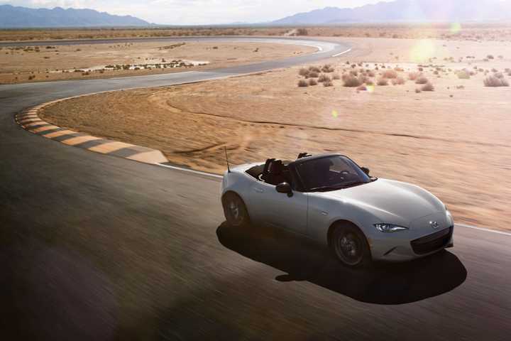 Dynamic front 3/4 shot of a silver 2024 Mazda MX-5 on a racetrack in the desert.