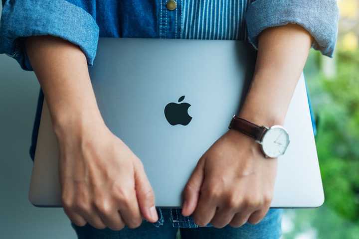 A woman standing and holding an Apple MacBook Pro laptop computer.