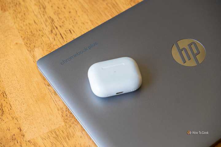AirPods Pro sitting on top of a Chromebook plus on a wooden table.