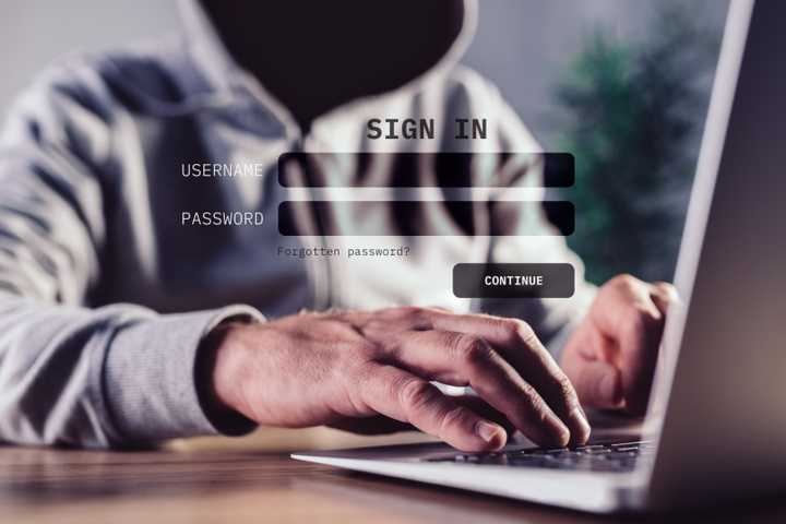 A dark hooded figure ominously using a laptop. 