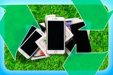 A pile of old phones on the grass with a recycling icon.