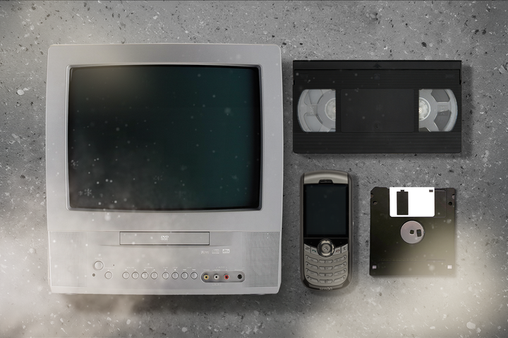 Old television, a VHS tape, an old cellphone, and a floppy disk, all placed on a dusty surface with light fog.